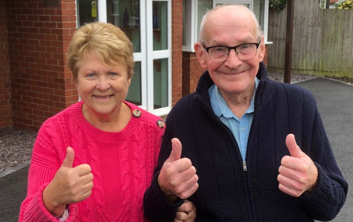 An elderly man and woman simling with their thumbs up
